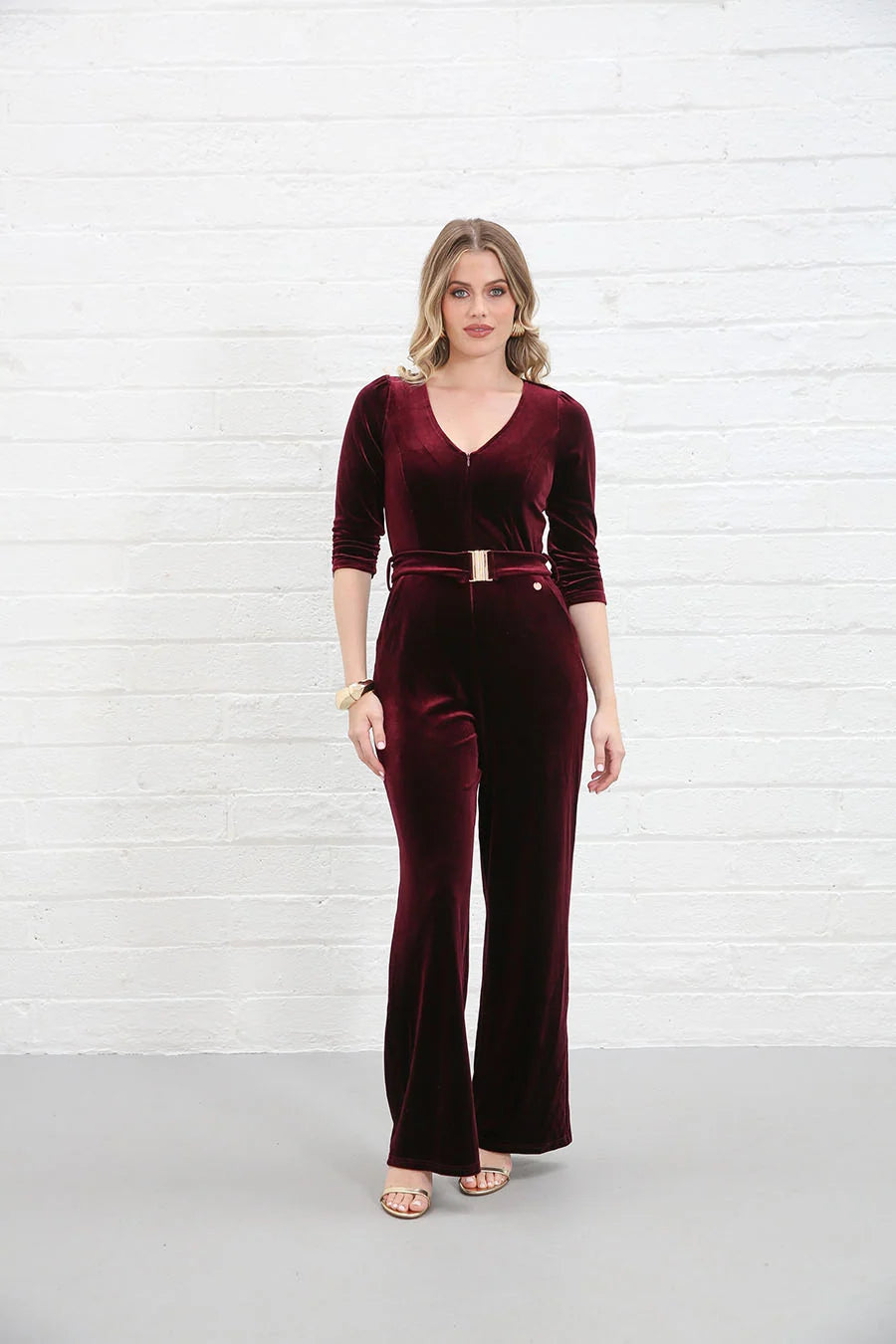 Rant & Rave Farrah Jumpsuit in wine velvet, front view worn by model with V-neck, zip front, gold belt and flared legs