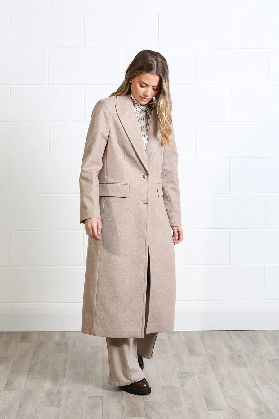 Rant & Rave Olivia Coat in biscuit, full - length front view worn by a model with a striped shirt and wide - leg trousers
