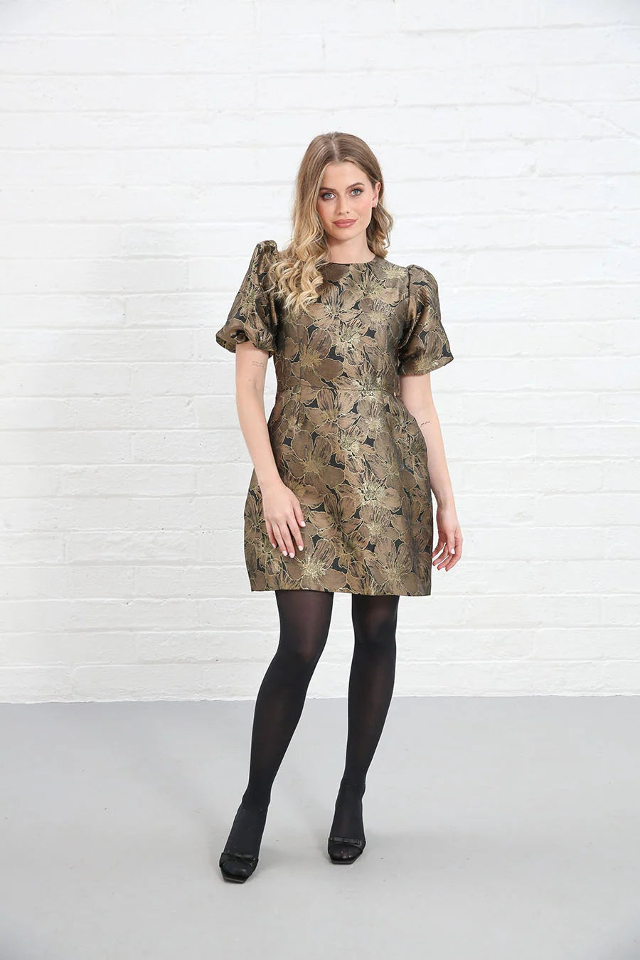 Rant & Rave Evelyn Dress in black and gold floral jacquard, front view worn by model with one hand on thigh.
