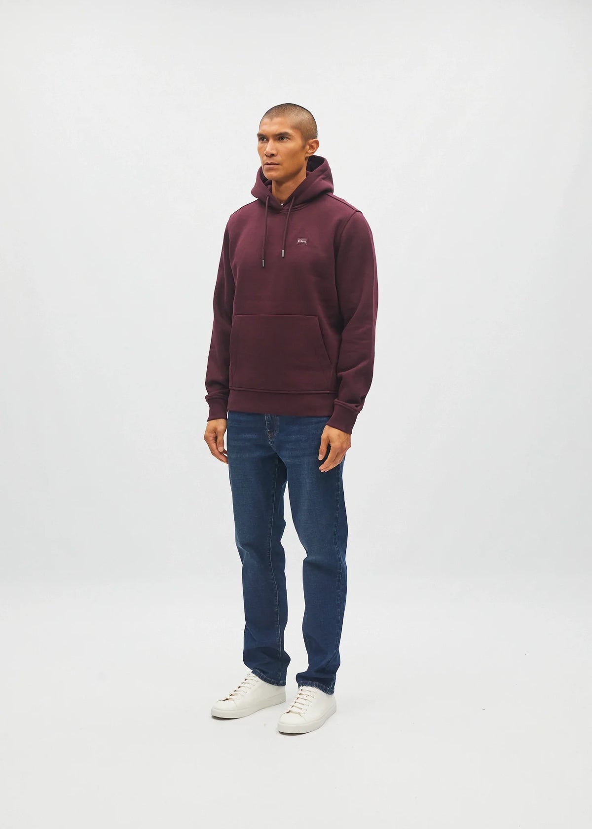 Diesel Julian hoodie in deep burgundy, angled model view with jeans and white sneakers