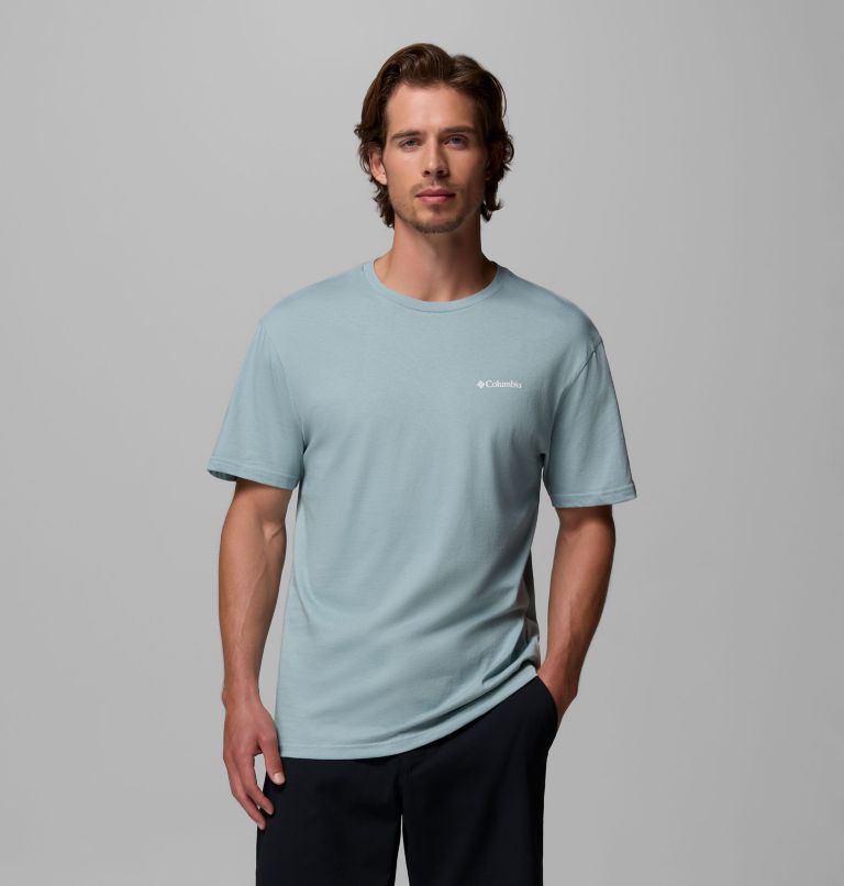 Man wearing a light blue t-shirt with a brand logo on a gray background