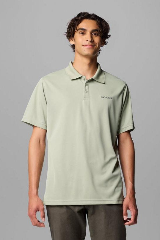 Man wearing a light green polo shirt with a brand logo on a gray background