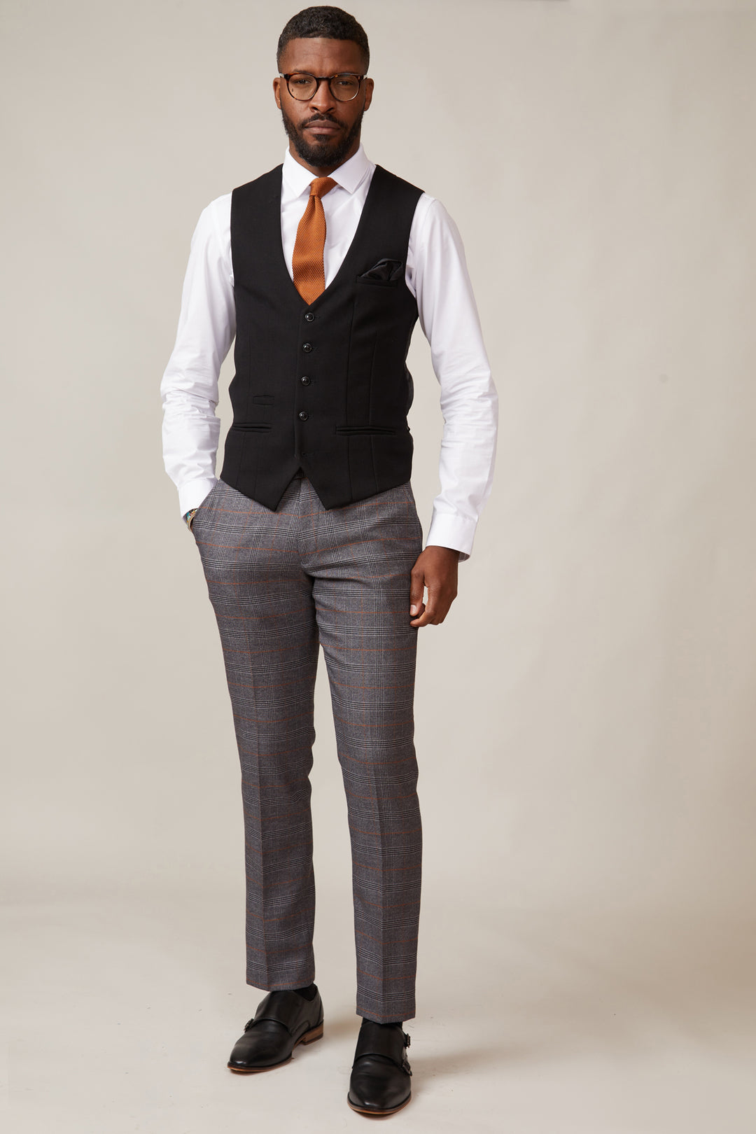 Man wearing a formal outfit with a black waistcoat, gray pants, and a white shirt.