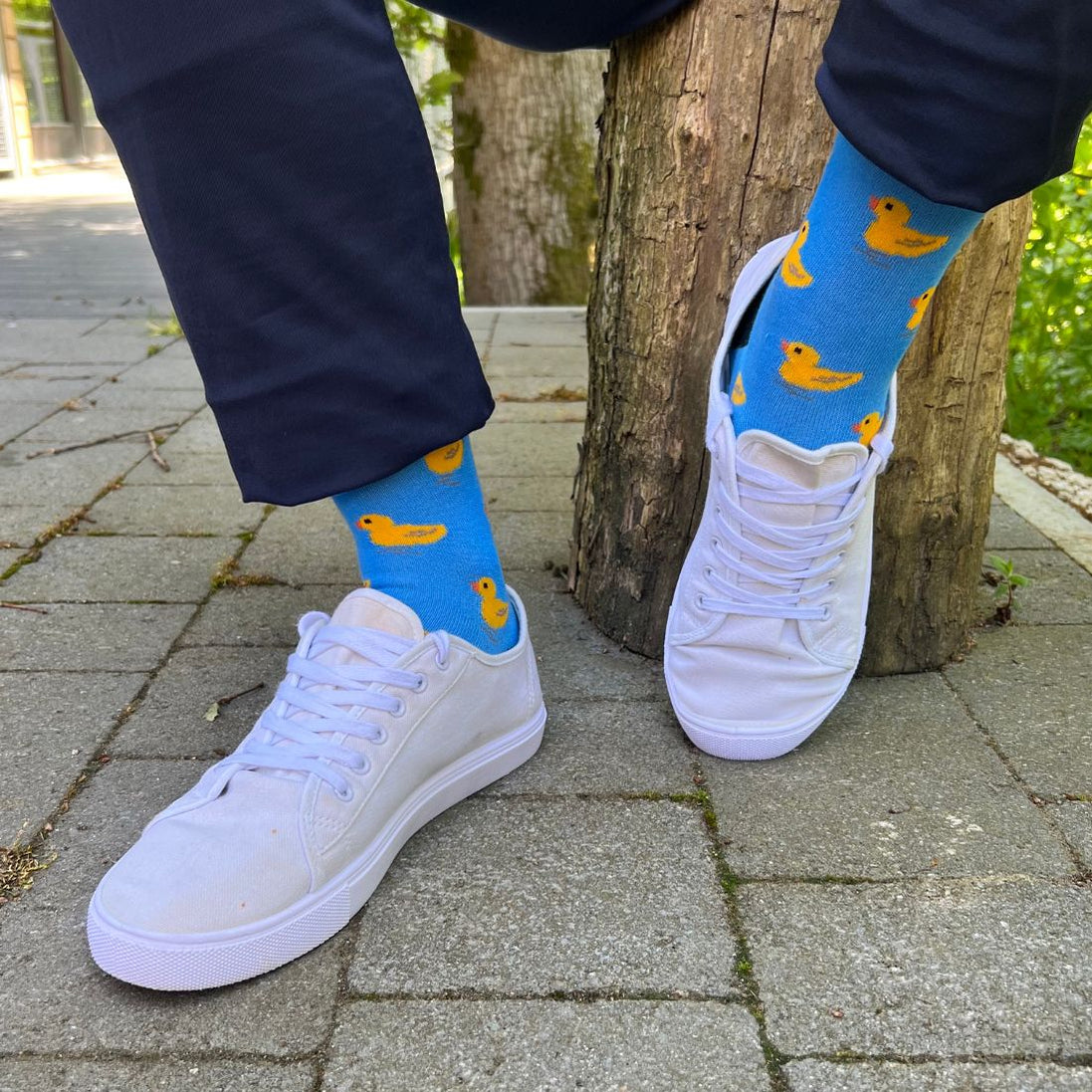 Person wearing blue socks with duck pattern and white sneakers on a paved surface.