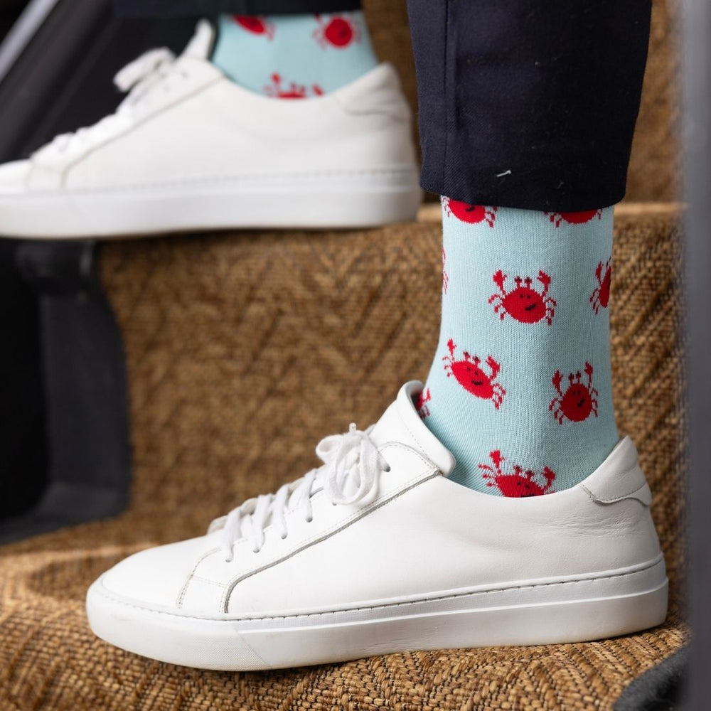 White sneakers with light blue socks featuring red crab patterns on a textured surface.
