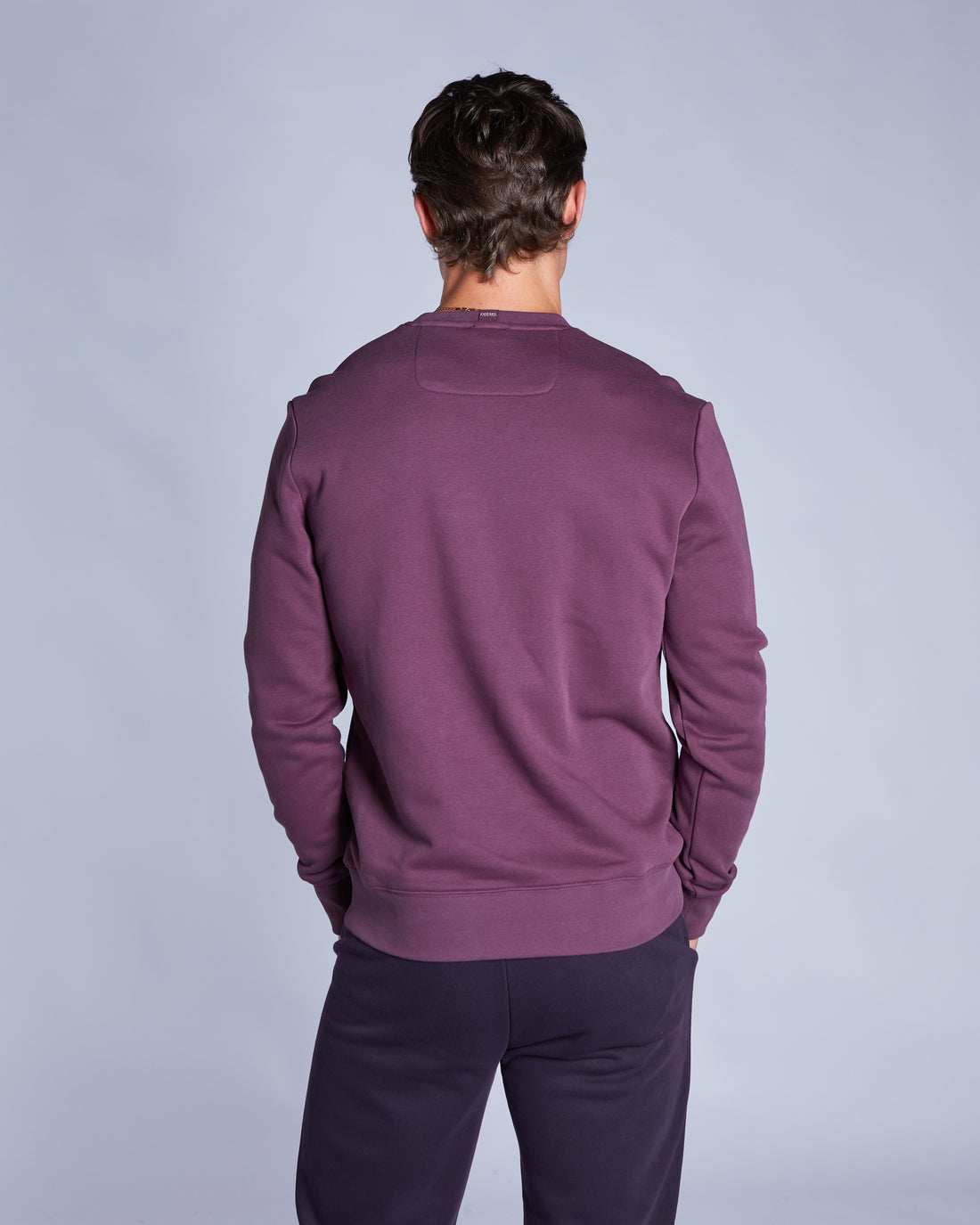 Person wearing a purple sweater and pants on a light gray background