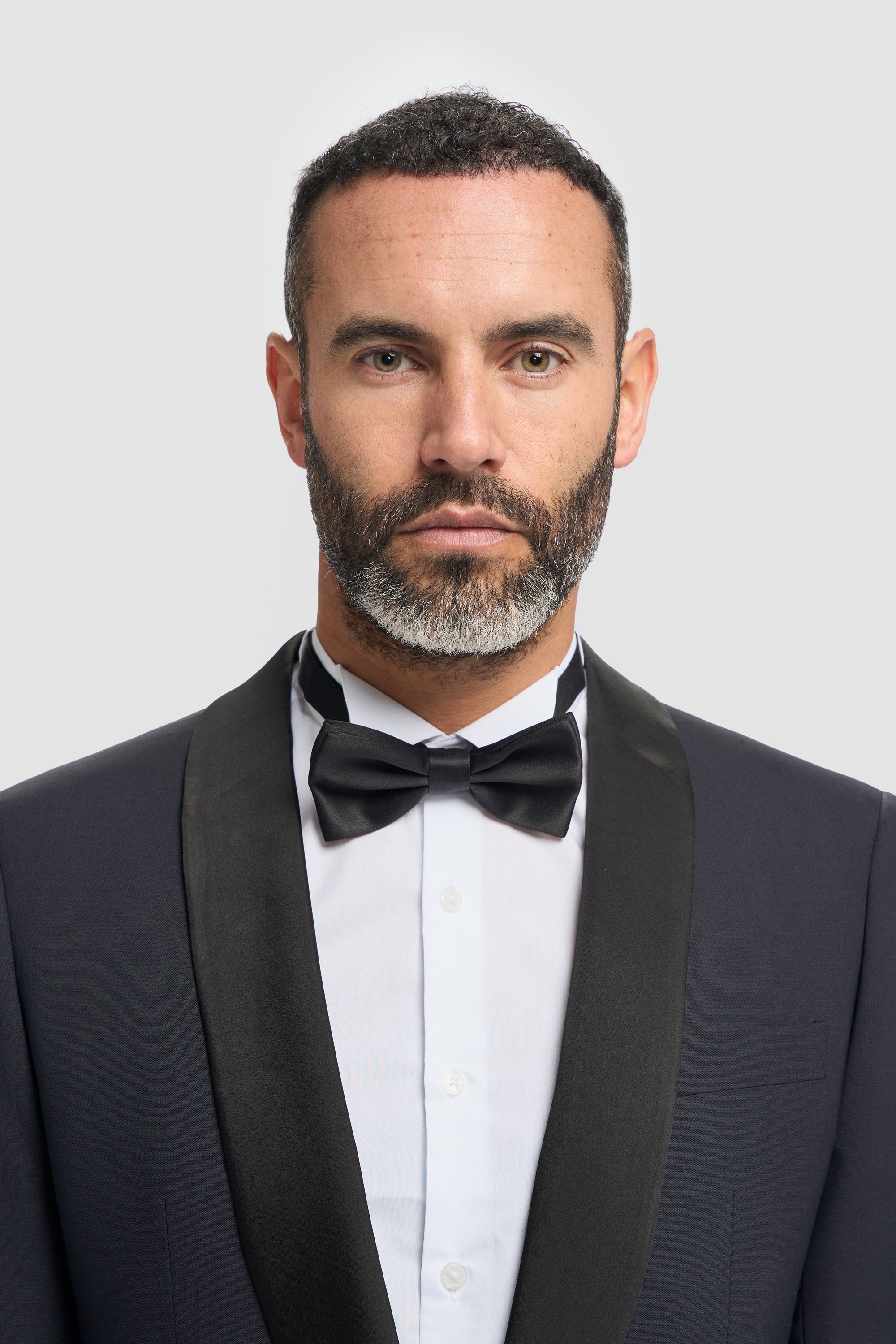 Man wearing a dark navy tuxedo with a bow tie against a light gray background