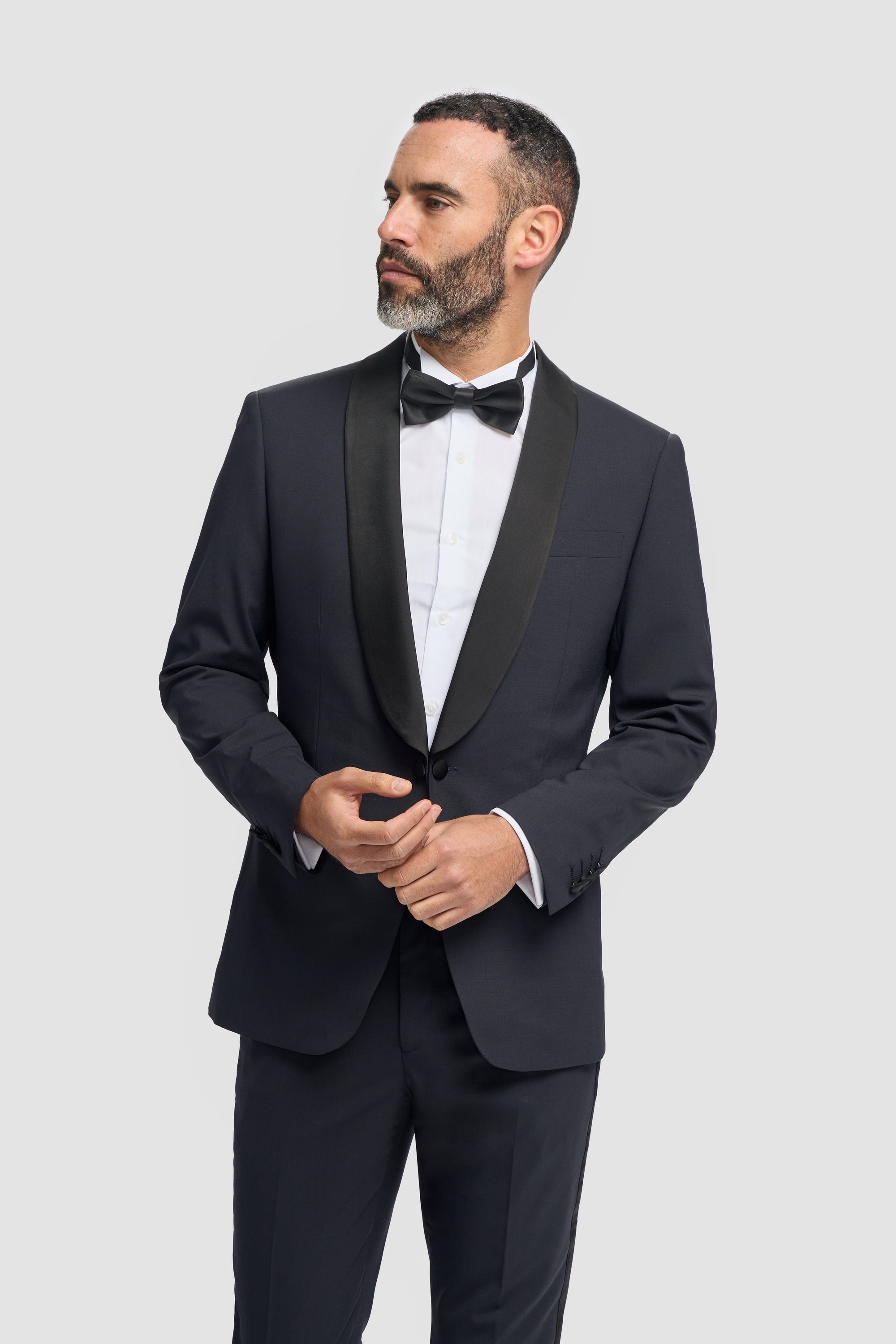 Man wearing a dark navy tuxedo with a bow tie on a light gray background