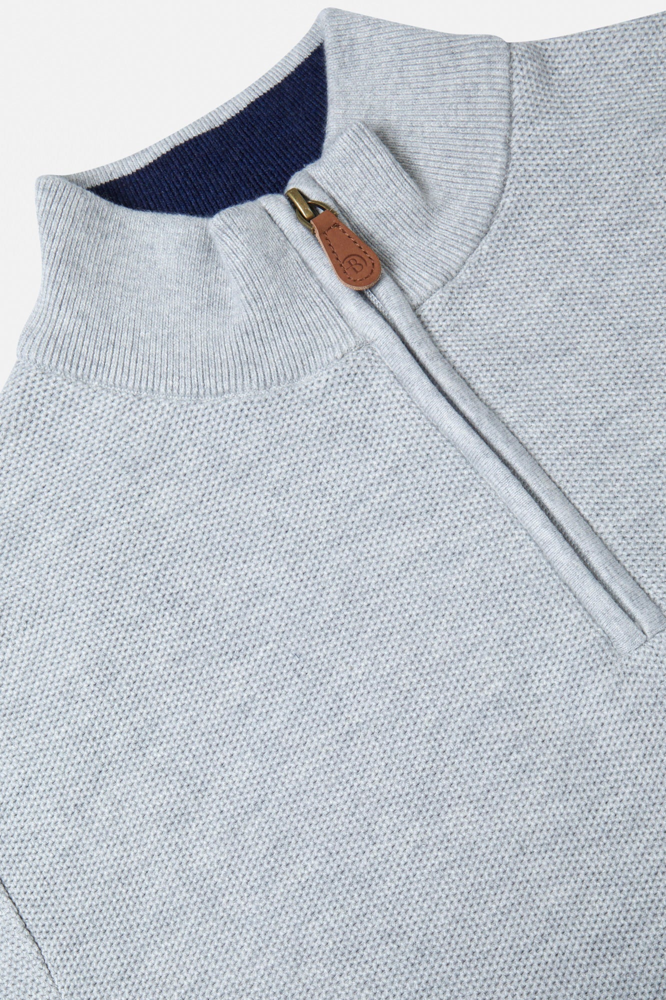 Close-up of a light gray sweater with a zipper and brown leather pull tab.
