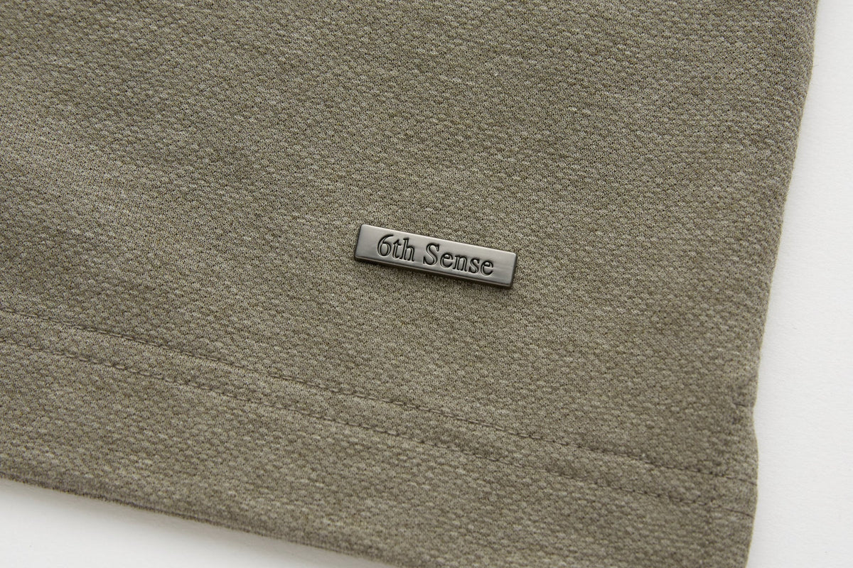 Rectangular metal 6th Sense logo badge on the lower hem of the brindle Evoke Polo.