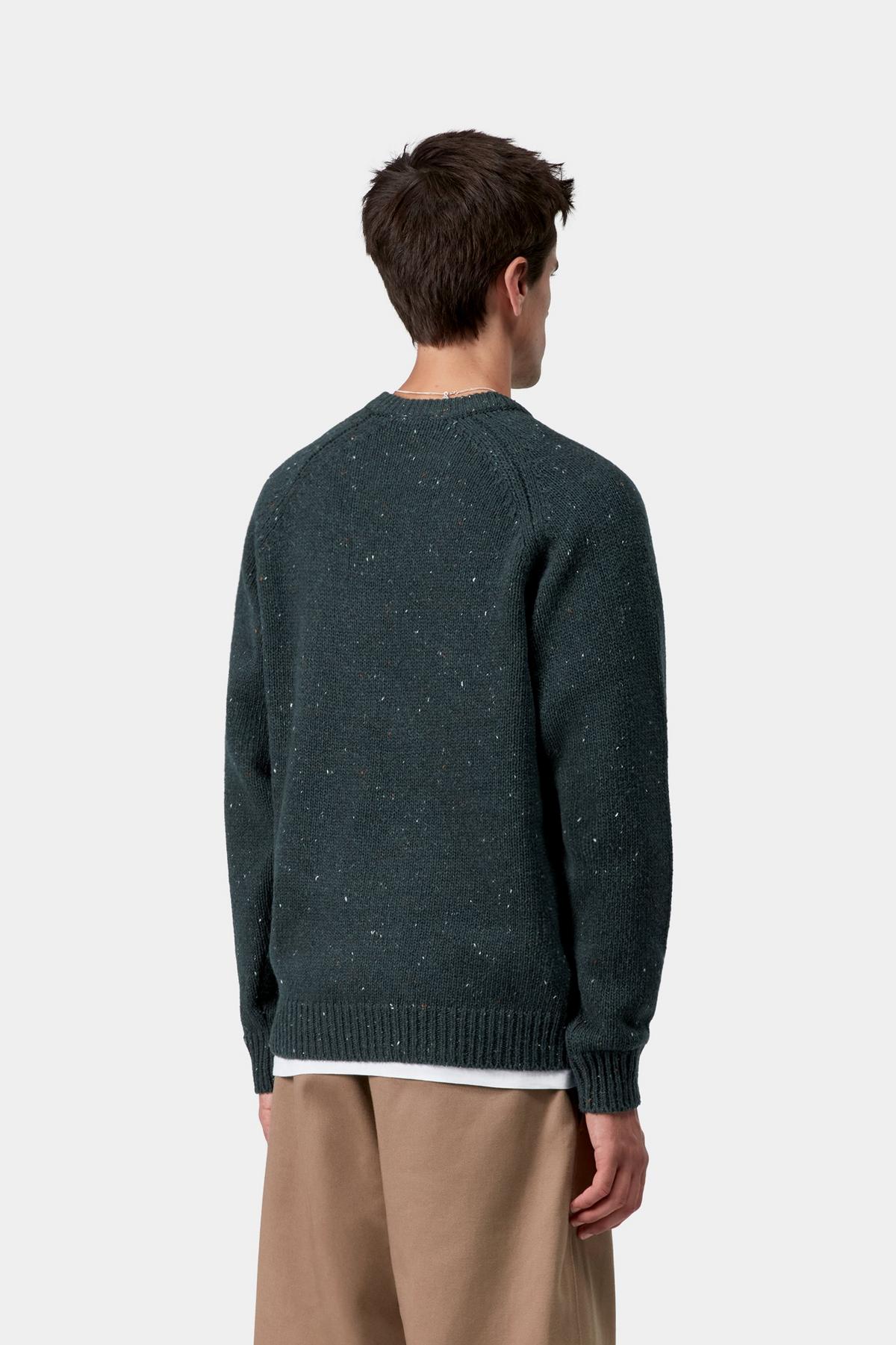 Person wearing a dark green sweater and beige pants on a white background