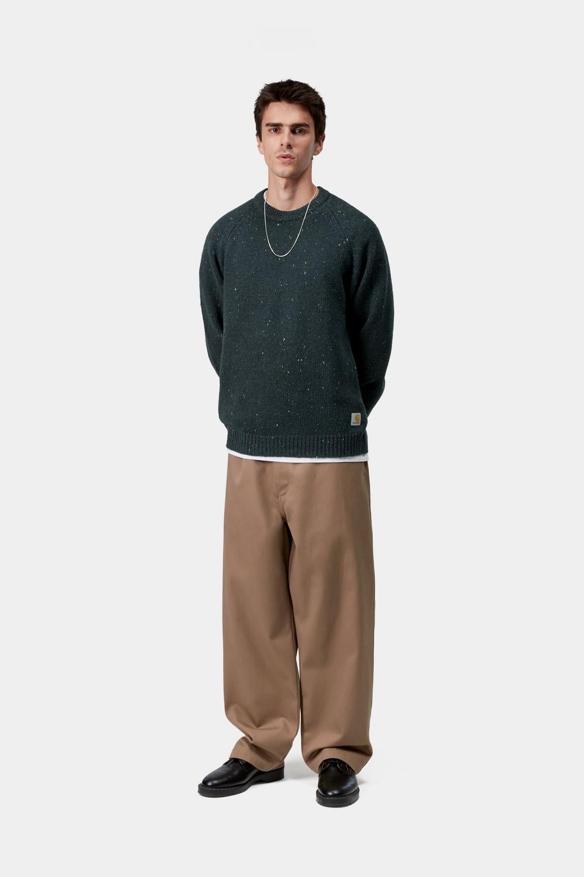 Man wearing a dark green sweater and beige pants on a white background