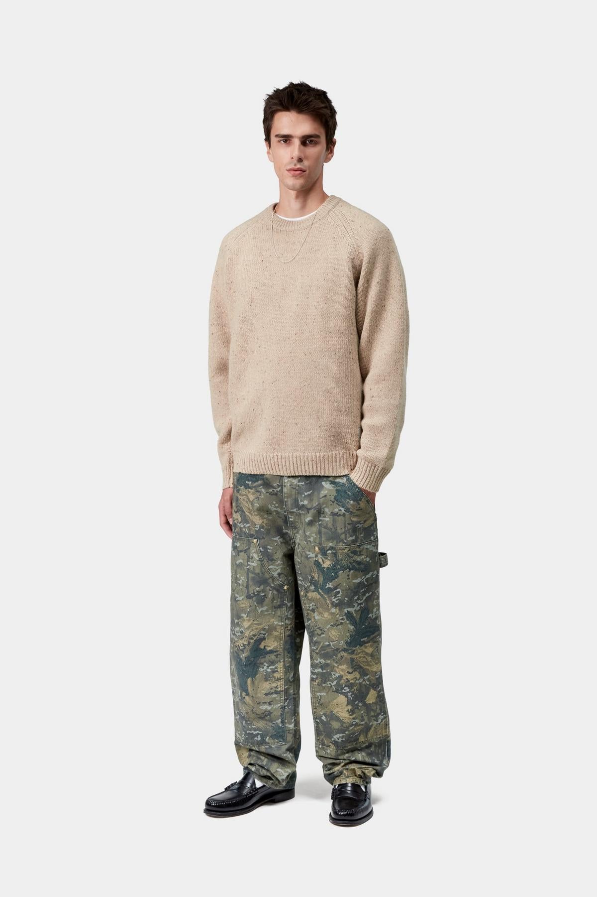 Man wearing a beige sweater and camouflage pants on a white background