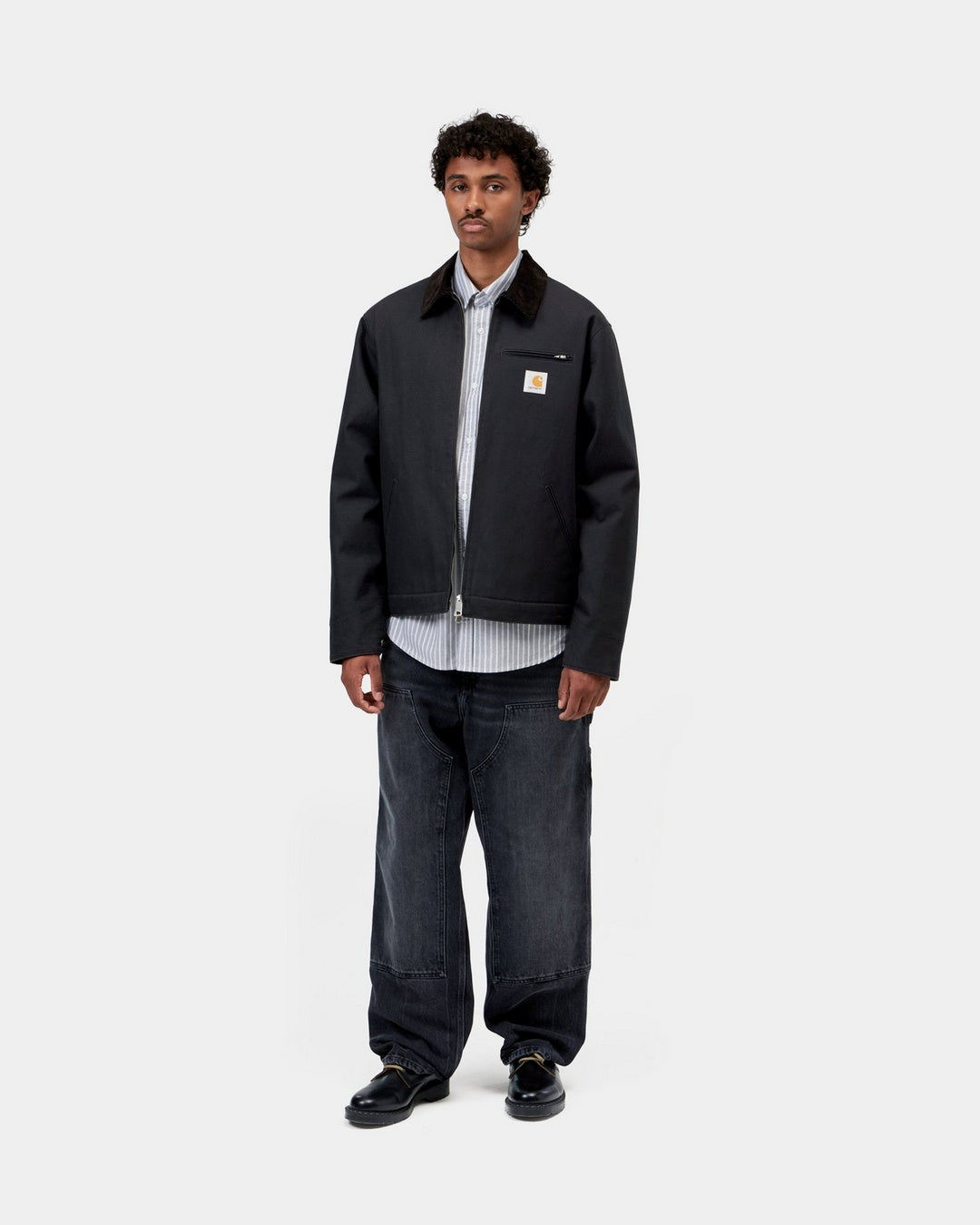 Carhartt WIP Detroit Jacket in Dark Navy / Black, worn open on a model with corduroy collar and chest logo patch.