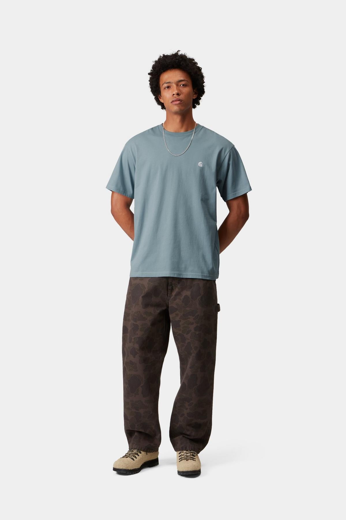 Man wearing a light blue t-shirt with a small logo on a white background