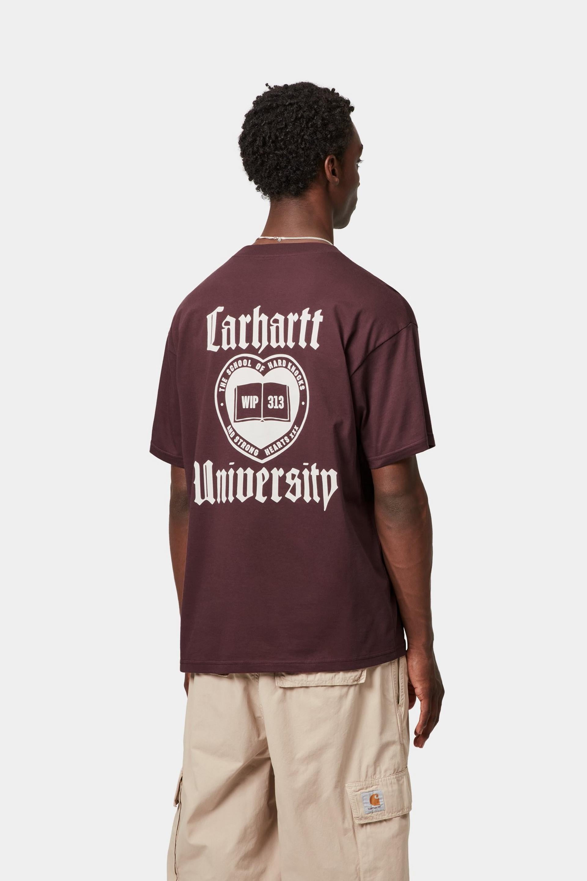 Person wearing a maroon t-shirt with 'Carhartt University' print on the back, standing against a white background.