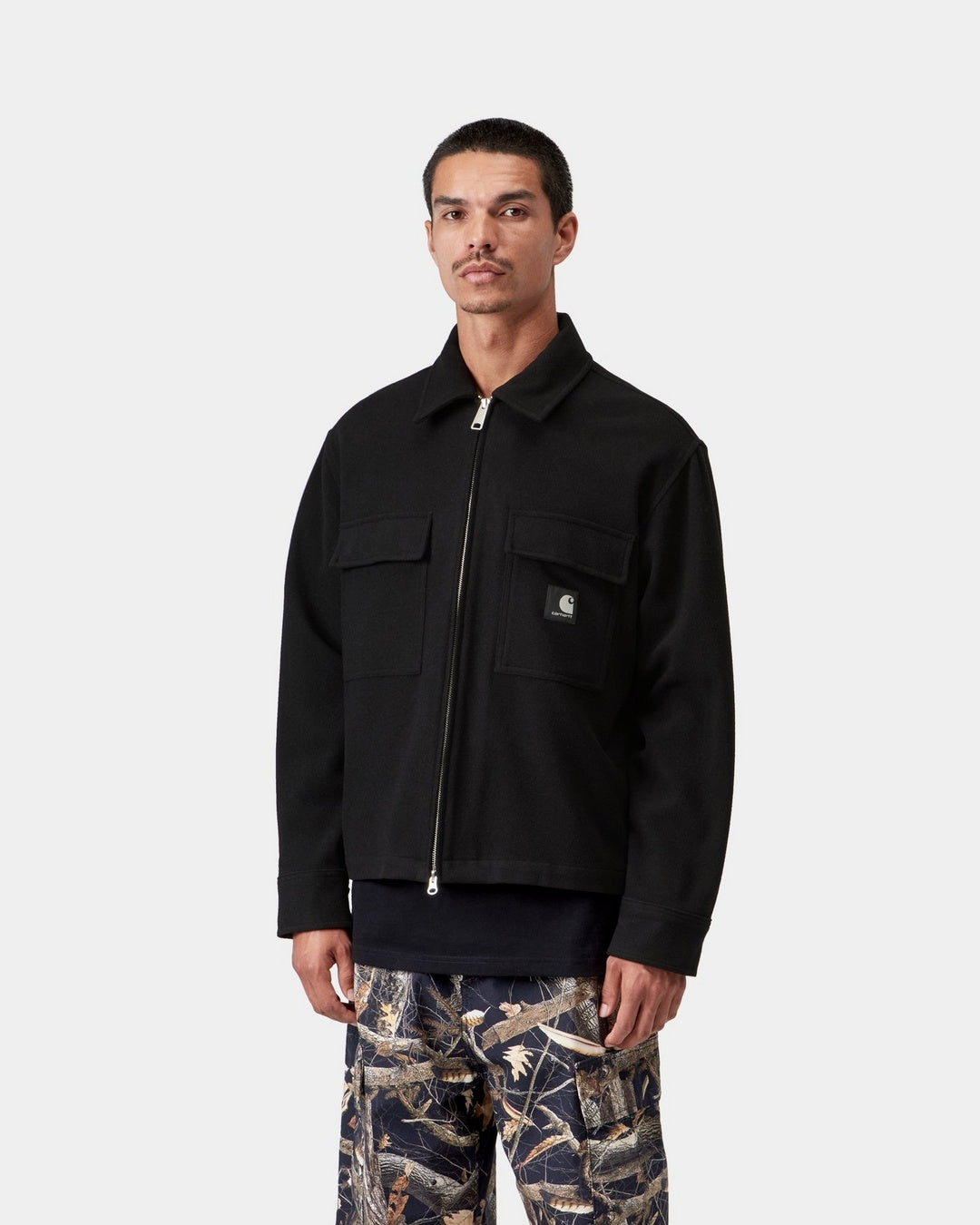 Carhartt WIP Atoka Shirt Jac in Black, front view on a model. The zip-up shirt jacket features a pointed collar, two chest flap pockets, a silver two-way zip, and a black Square Label on the left pocket.