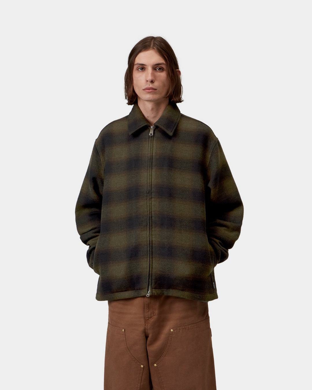 Front view of a model wearing the Carhartt WIP Alton Jacket in Alton Check, Cypress, a zip-front style with a pointed collar, two side welt pockets, and an allover check pattern.