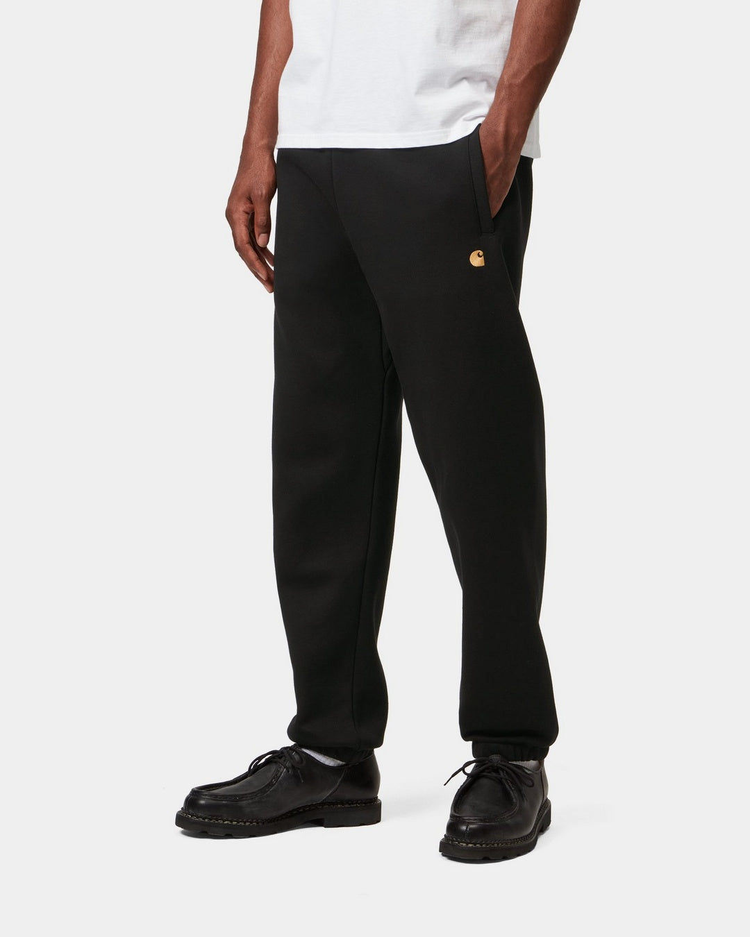 Carhartt WIP Chase Sweat Pant in Black / Gold, shown on model with embroidered gold C logo on the front.