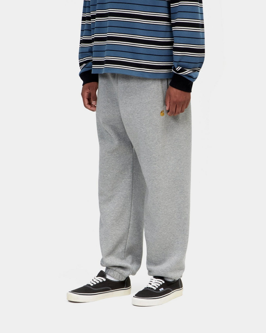 Carhartt WIP Chase Sweat Pant in Grey Heather / Gold, shown on model in a front view with embroidered logo and elasticated cuffs.