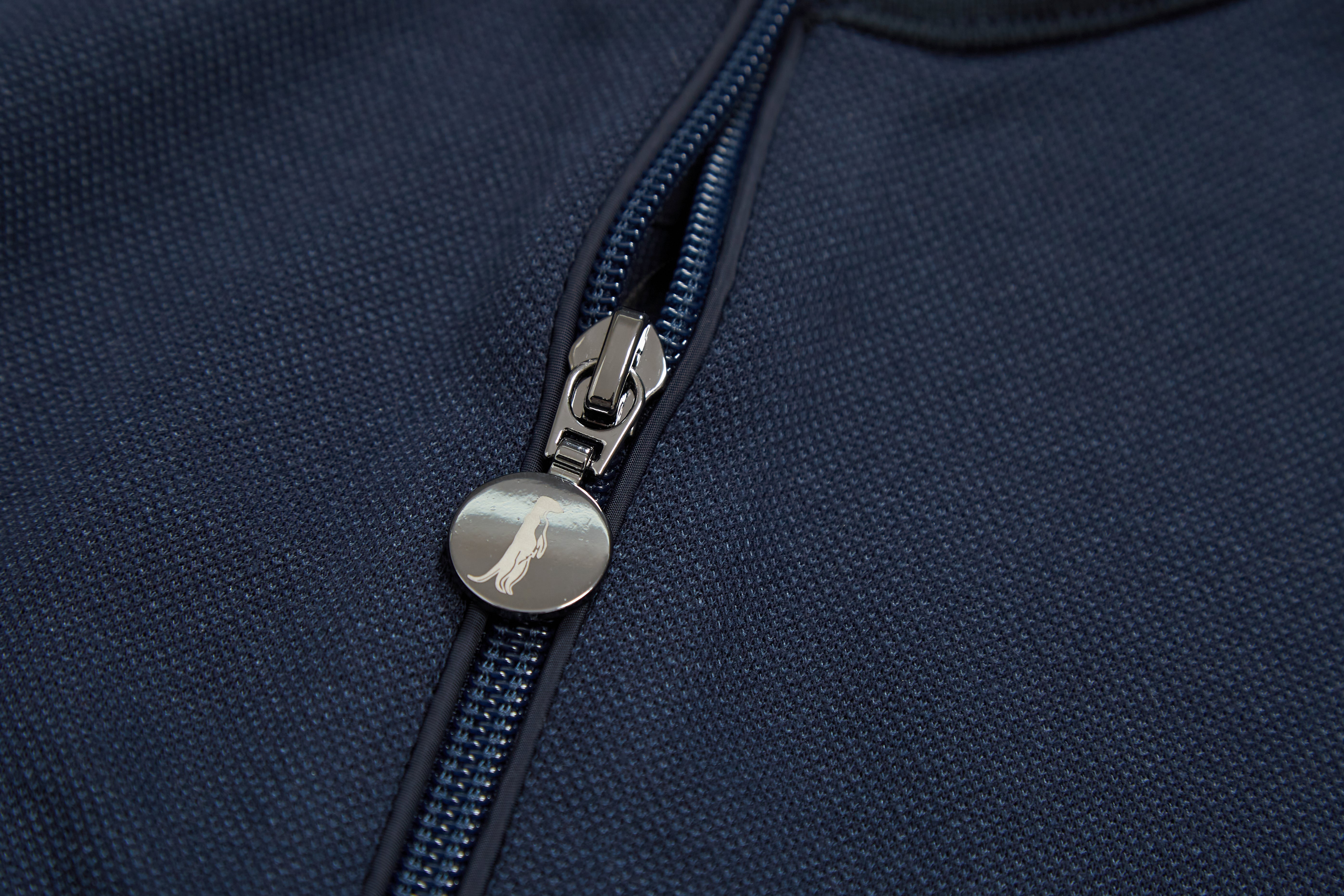 Close-up of a navy blue jumper with a zipper and silver emblem.