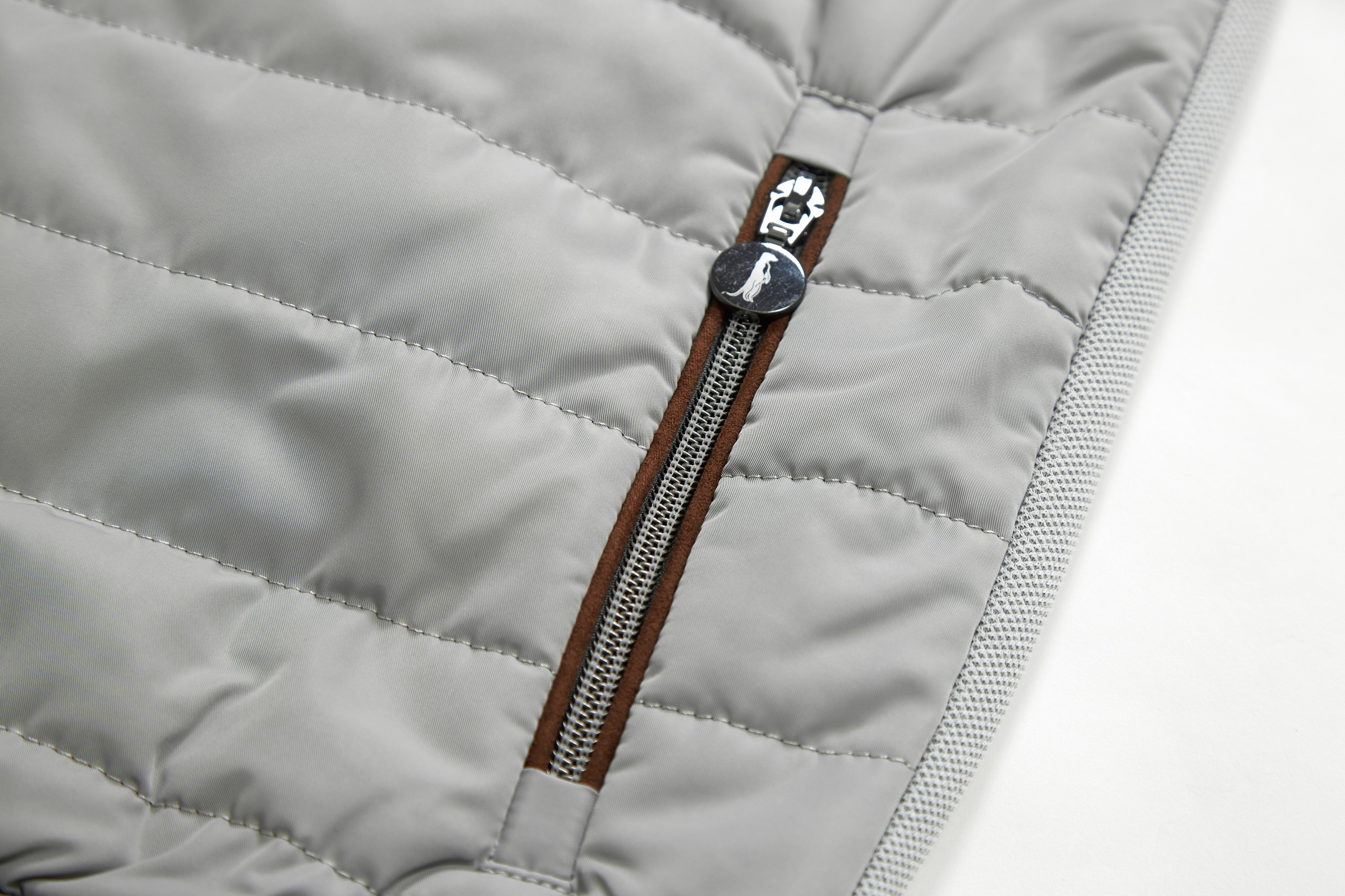 Close-up of a quilted jacket with a brown zipper and decorative button on a light gray background