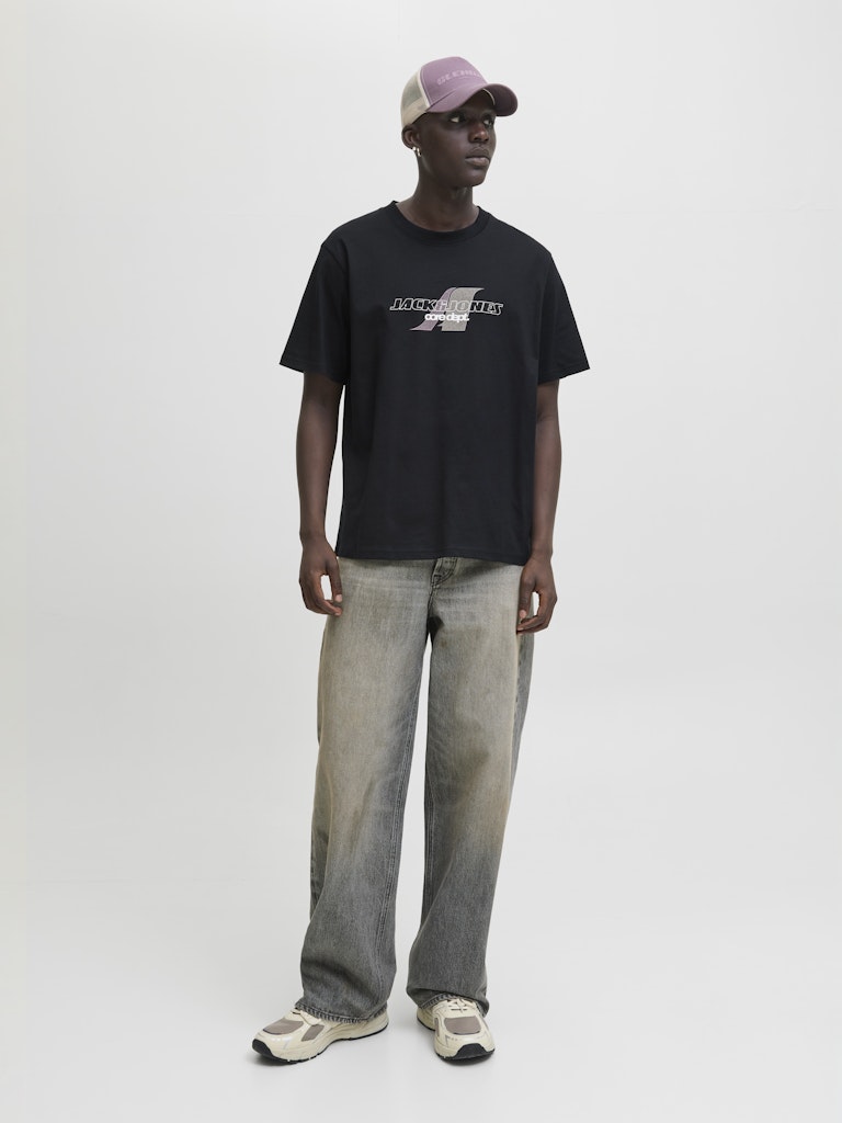 Person wearing a black t-shirt with a logo and light-colored pants on a white background