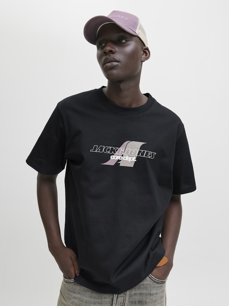 Person wearing a black t-shirt with a logo and text, standing against a plain background