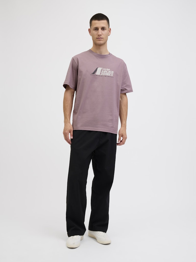 Person wearing a mauve t-shirt with a logo and black pants on a white background