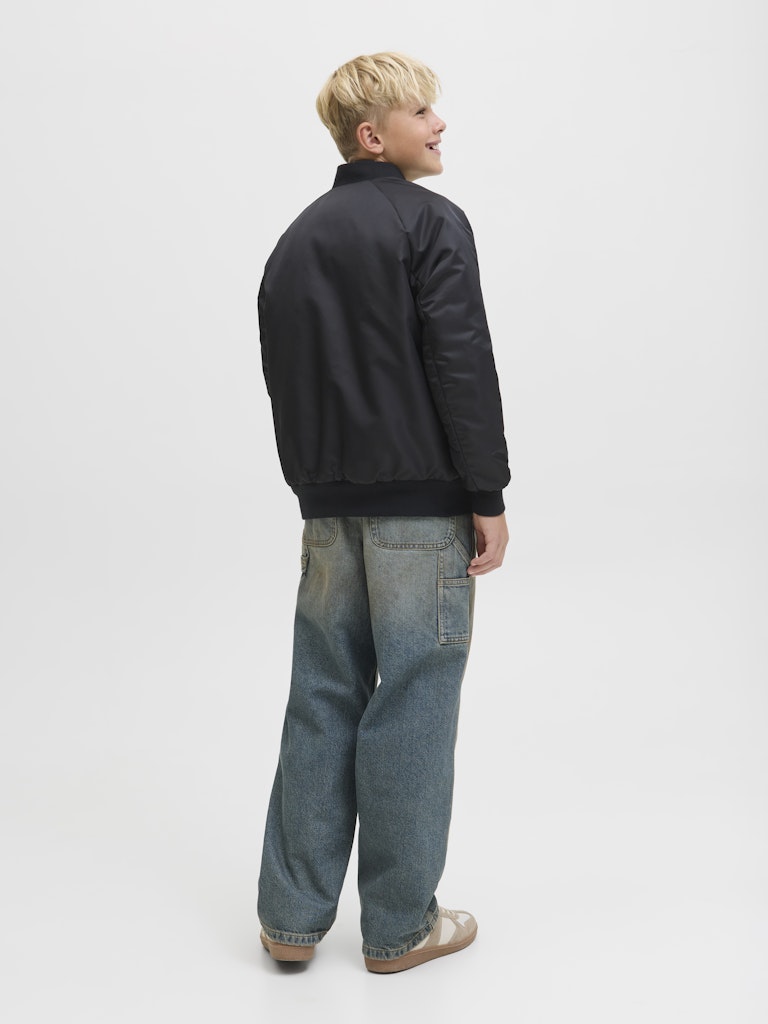 Side view of the junior boys black bomber jacket with blue jeans