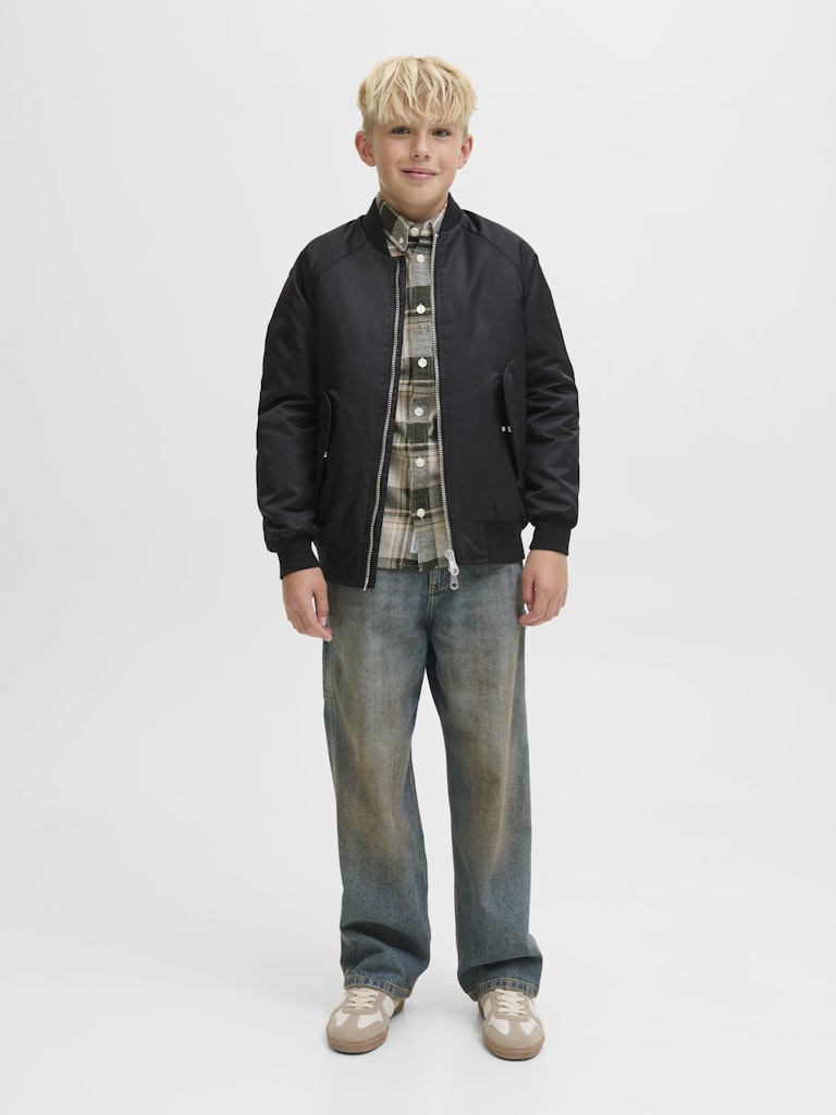 Young boy wearing a black jacket, plaid shirt, and jeans on a white background