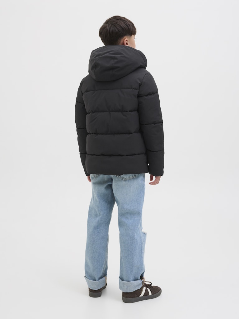 Person wearing a black puffer jacket and light blue jeans on a white background