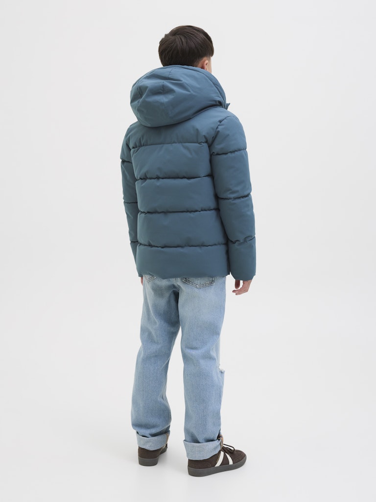 Person wearing a blue puffer jacket and jeans on a white background
