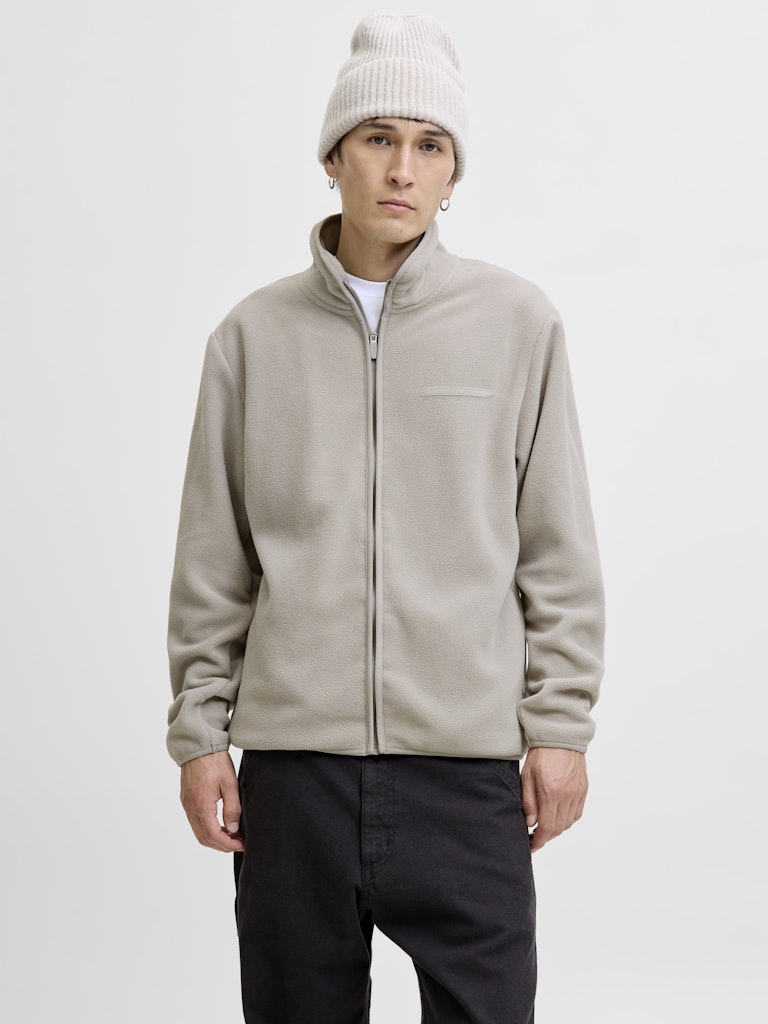 Person wearing a beige jacket and white beanie on a plain background