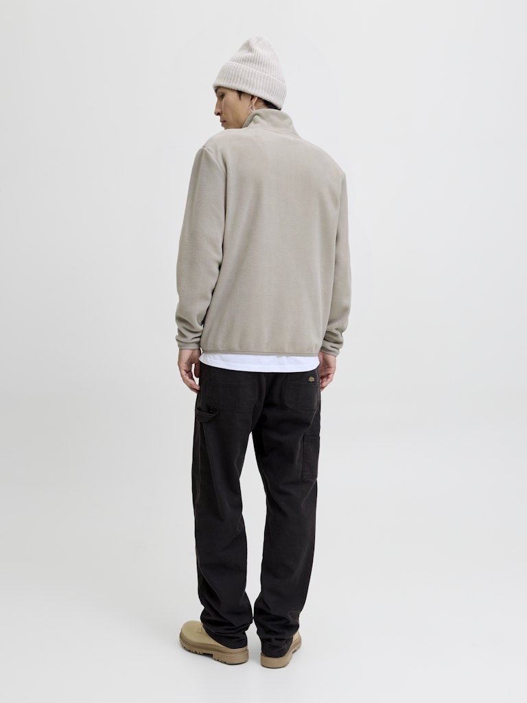 Person wearing a beige half-zip sweatshirt, black pants, and a white beanie on a white background