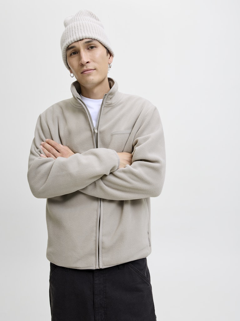 Person wearing a beige jacket and white beanie on a plain background