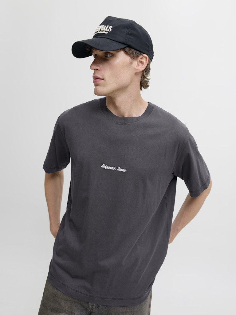 Man wearing a dark gray t-shirt with a logo and a black cap on a light gray background