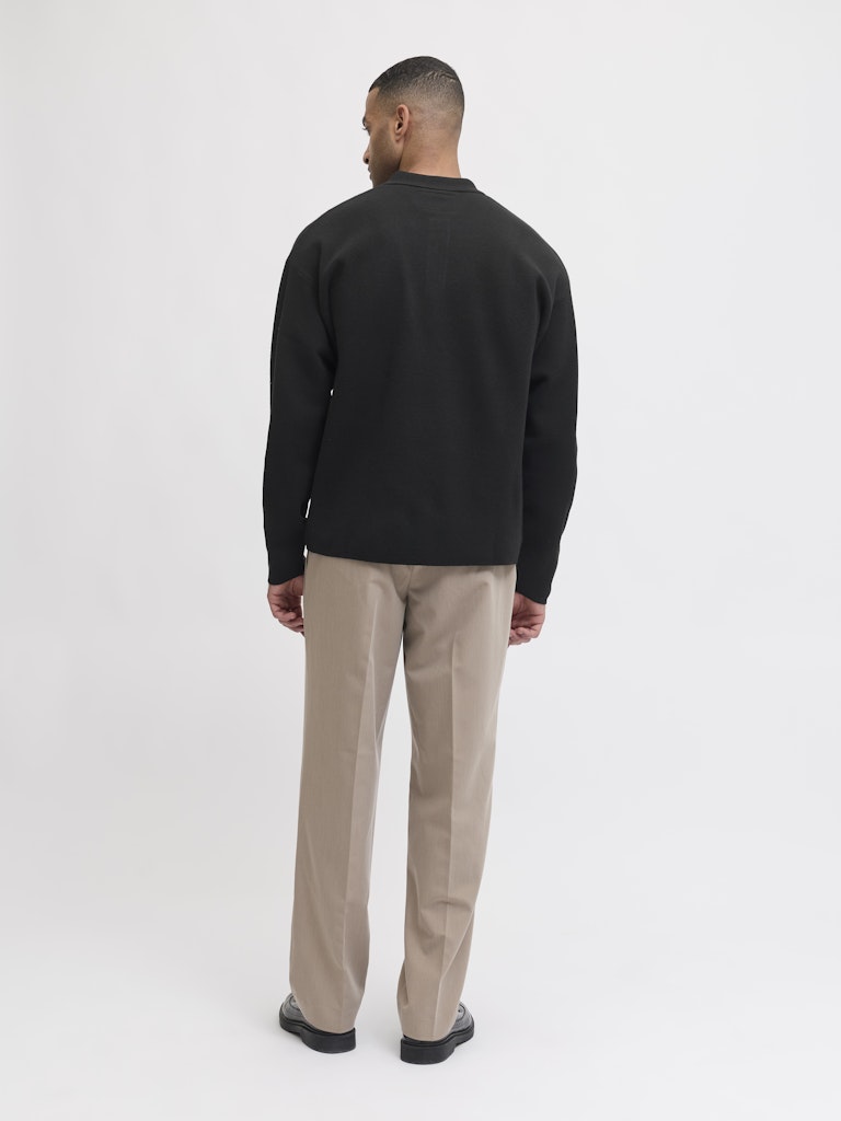 Man wearing a black sweater and beige pants on a white background