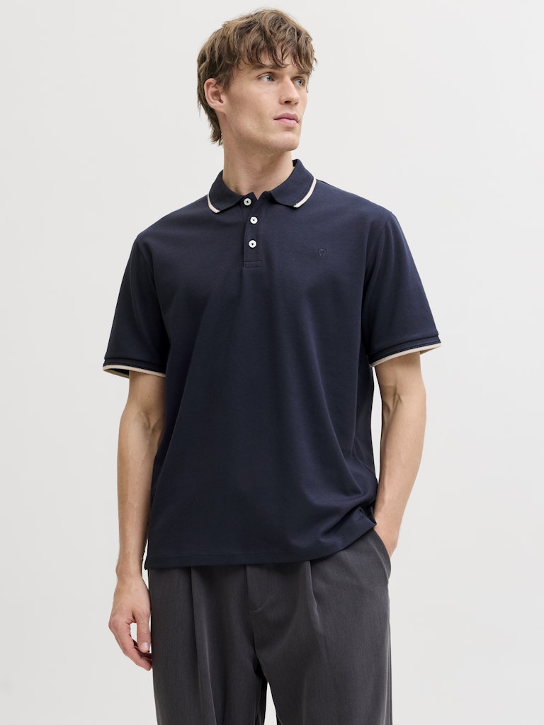 Man wearing a navy polo shirt with white trim on a light gray background