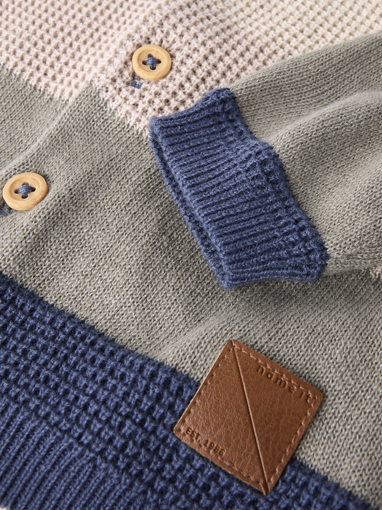 Close-up of a knitted garment with buttons and a brand label.