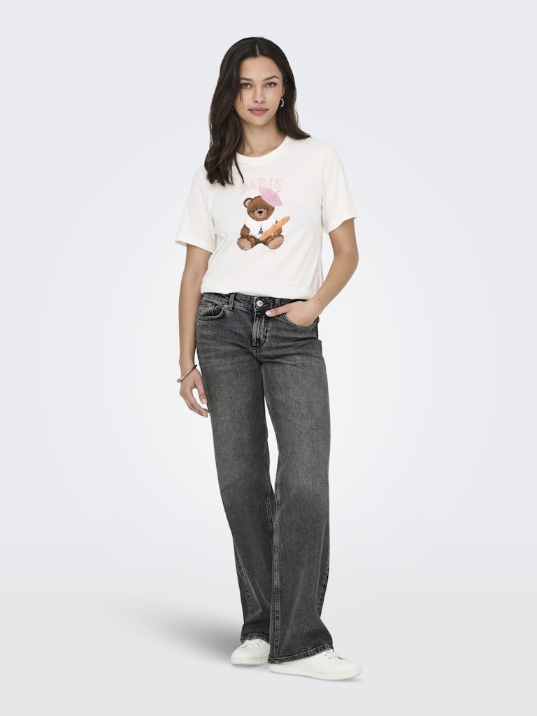Woman wearing a white t-shirt with a teddy bear graphic and dark jeans on a white background