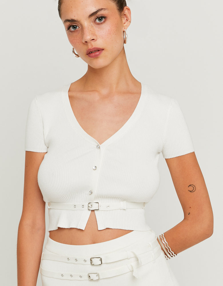 Woman wearing a white cropped top with buttons and a matching skirt on a plain background