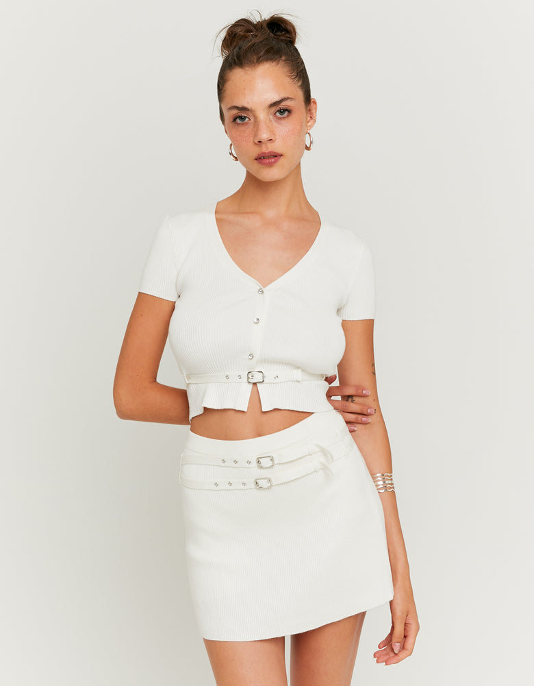 Woman wearing a white outfit with a belt on a plain background