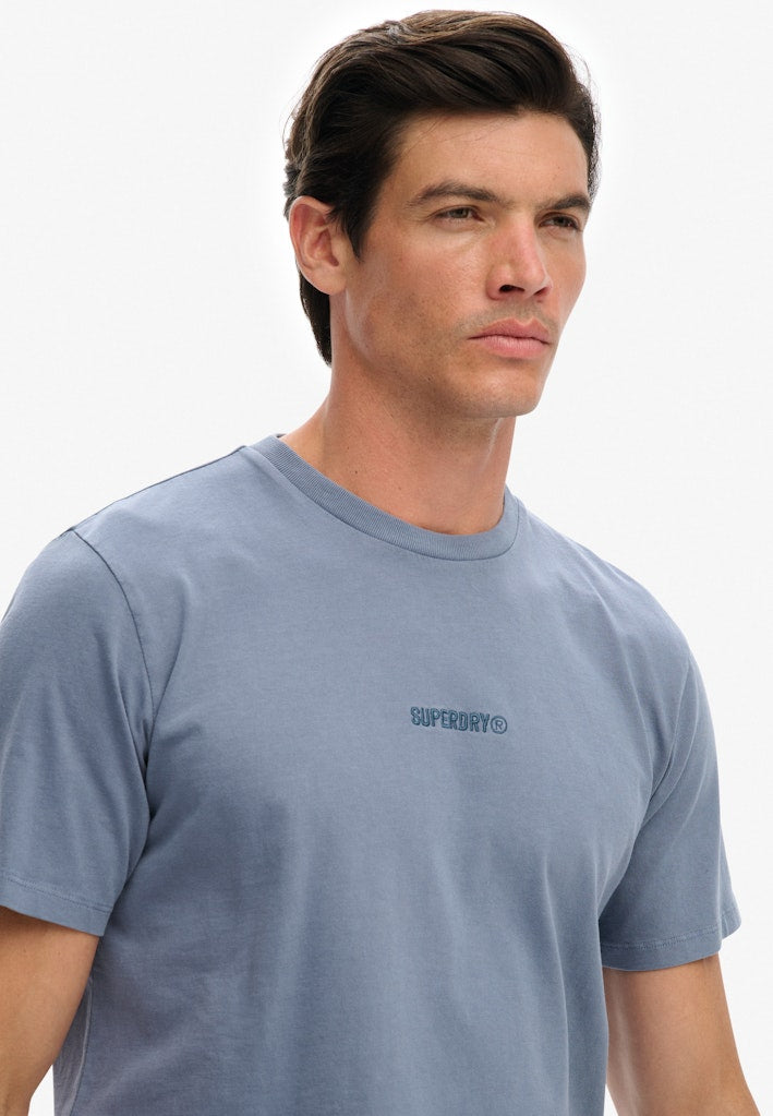 Man wearing a blue t-shirt with a logo on a plain background