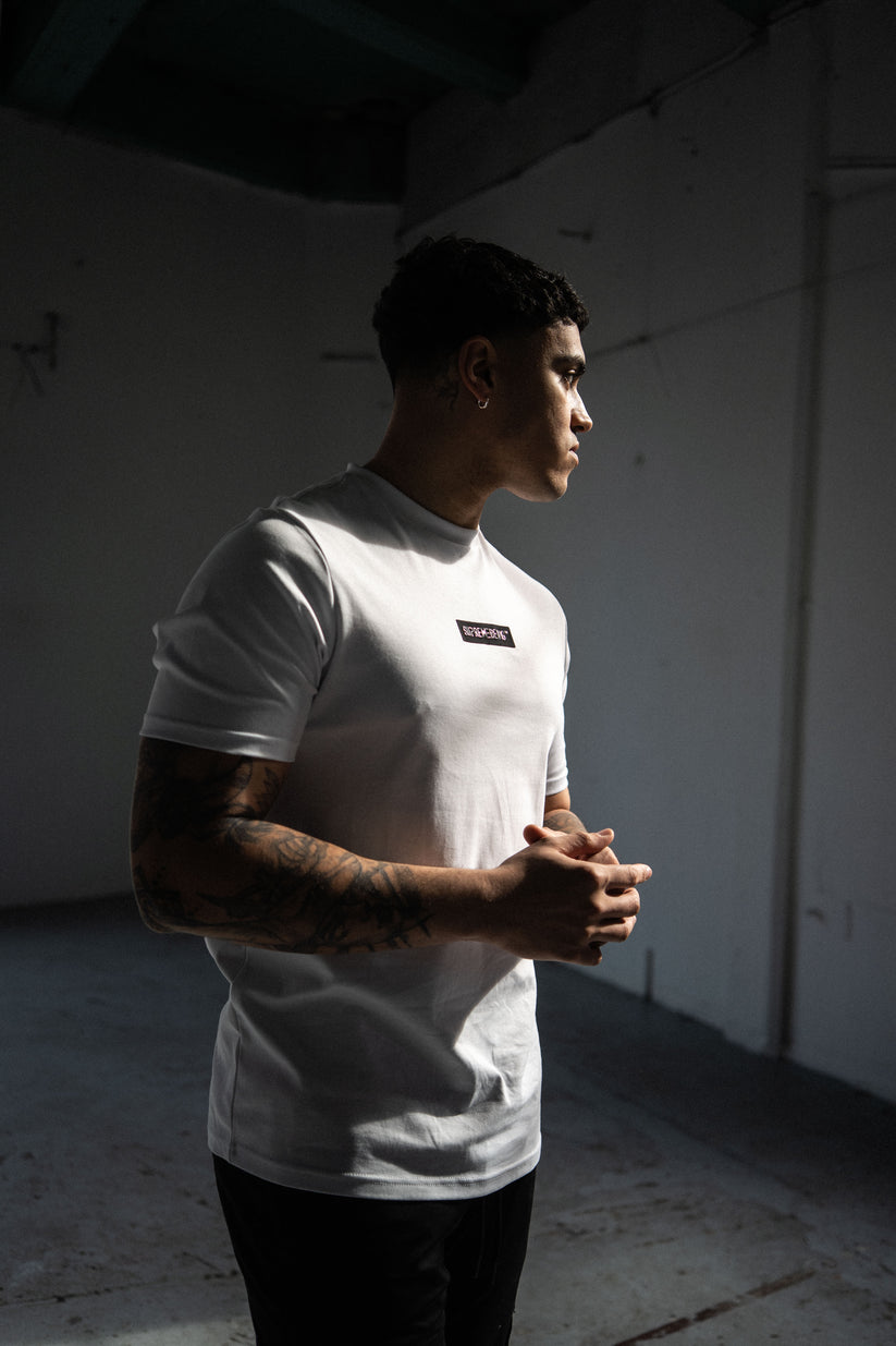 Person wearing a white t-shirt with a small logo in a dimly lit room.