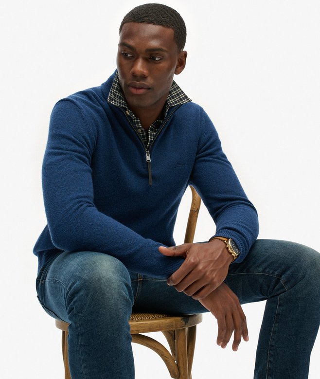 Man wearing a blue sweater and jeans sitting on a chair against a white background