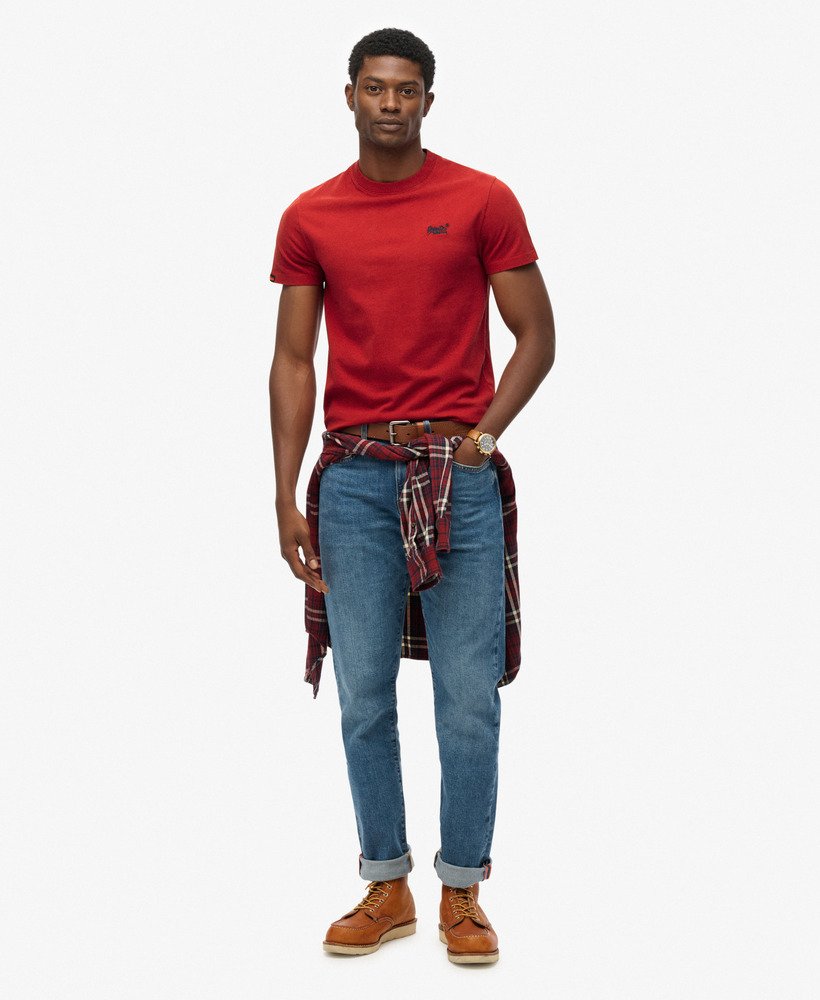 Man wearing a red t-shirt, blue jeans, and brown boots on a white background