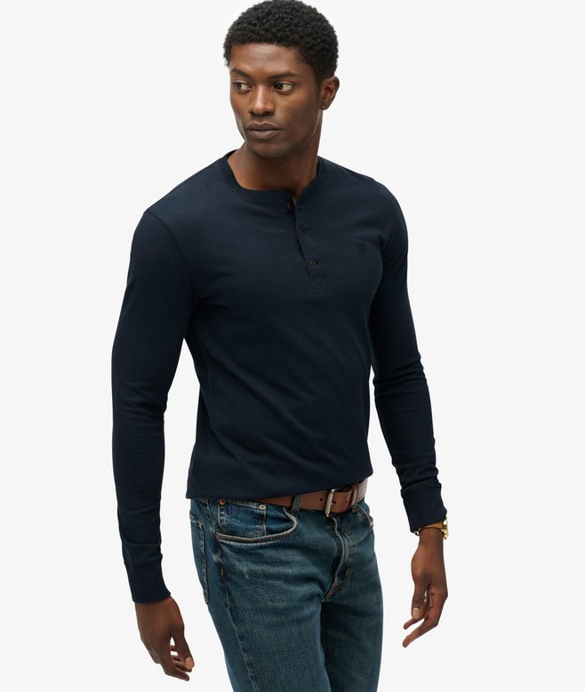 Man wearing a navy long-sleeve henley shirt and jeans on a white background