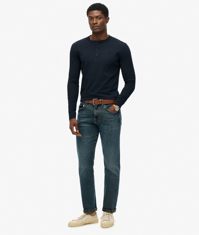 Man wearing a navy long-sleeve shirt and blue jeans on a white background