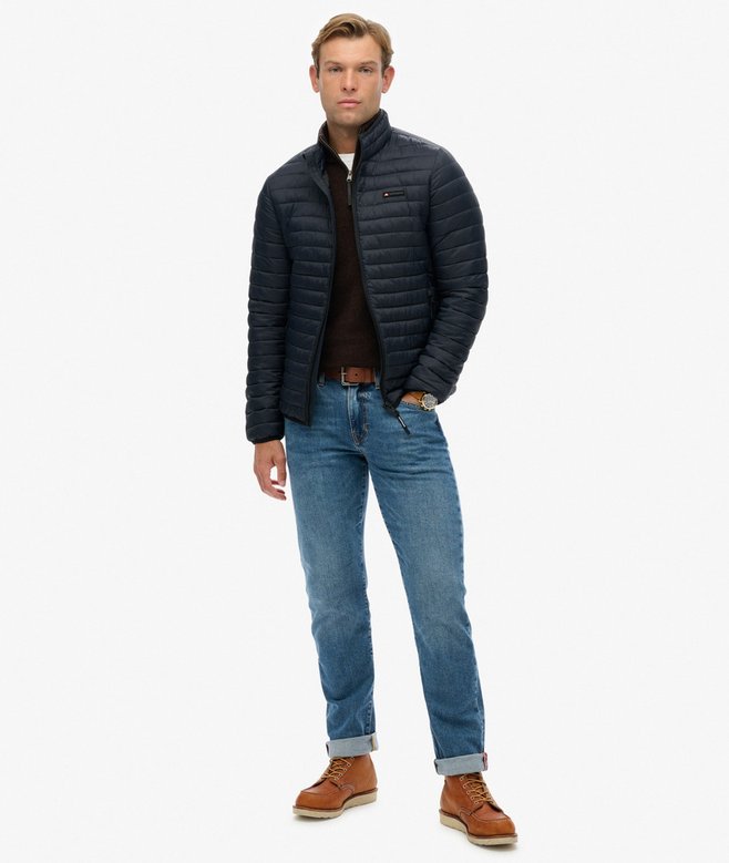 Man wearing a navy puffer jacket, brown knit, blue jeans, and brown boots on a white background